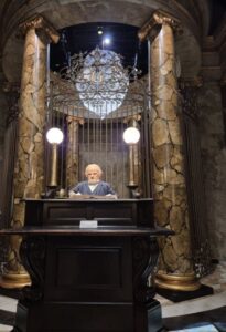 Gringotts Wizarding Bank scene with a goblin behind a desk, flanked by marble columns.