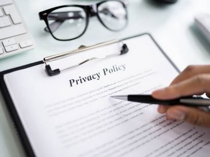 Hand holding a pen over a clipboard with a Privacy Policy document and eyeglasses nearby.