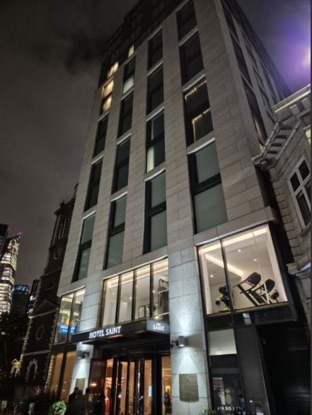 Exterior of Hotel Saint London illuminated at night with a well-lit lobby and visible gym area.