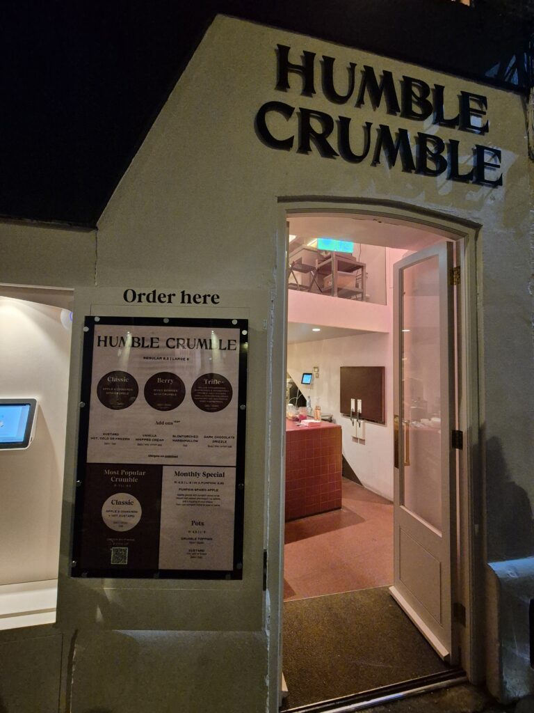 Entrance to Humble Crumble, featuring a sign above the door and a menu board with various crumble and drink options.