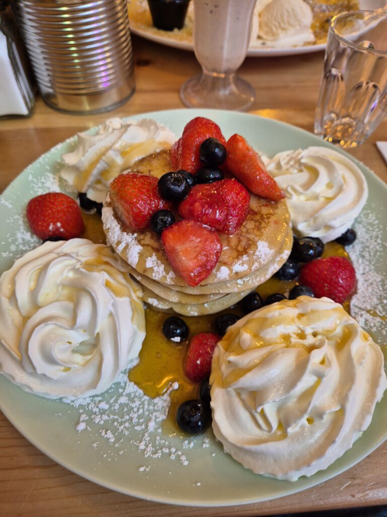 A plate of pancakes from My Old Dutch topped with fresh strawberries, blueberries, and whipped cream, drizzled with syrup.