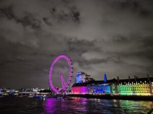 Night scene featuring the London Eye, illuminated in pink and purple lights against a dark sky.