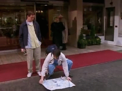Joey and Chandler from Friends in London, trying to figure out directions with a map spread out on the ground.