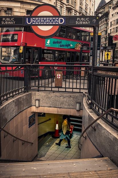 Entrance to a London Underground public subway station, part of the efficient London public transportation system, with a red double-decker bus in the background.