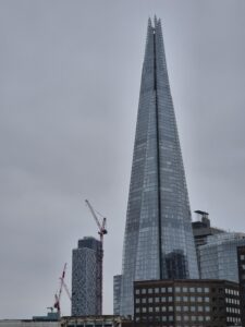 Modern skyscraper with a pointed tip and several tiers, photographed on a cloudy day.