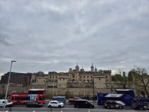 The Tower of London with a busy street in the foreground, including red double-decker buses.