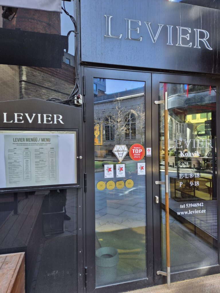 Entrance of Levier café with menu displayed on the left side and glass door with various stickers.