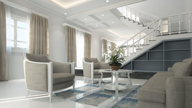 A modern living room with a minimalist design, featuring light gray armchairs, a matching sofa, a white coffee table with a potted plant, and an elegant staircase with white railings. Showing a minimalism lifestyle.