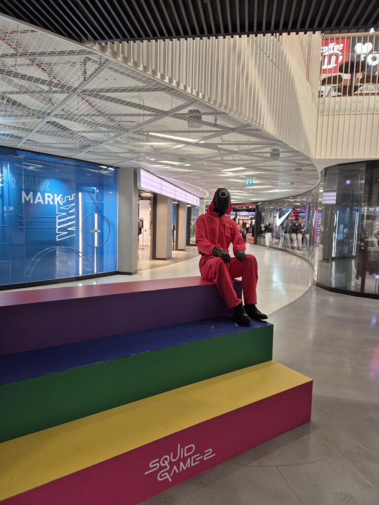 A mannequin dressed as a guard from Squid Game sitting on colorful steps inside Viru Keskus in Tallinn.