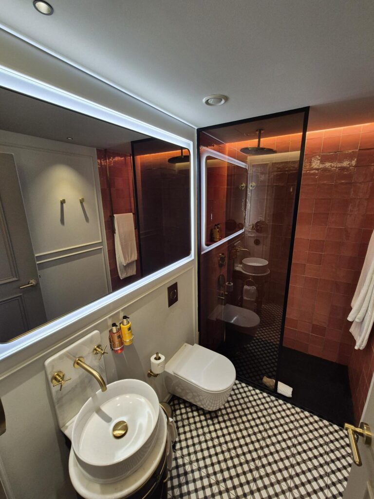 Modern bathroom in Upon Angels’ premium studio, featuring gold fixtures, patterned tiles, and a rainfall shower.