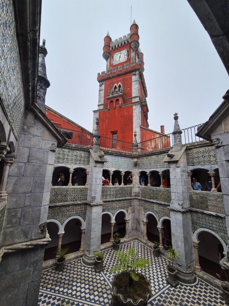 Close-up of a red tower at Pena Palace with arched windows and ornate stonework, part of a larger historic structure.