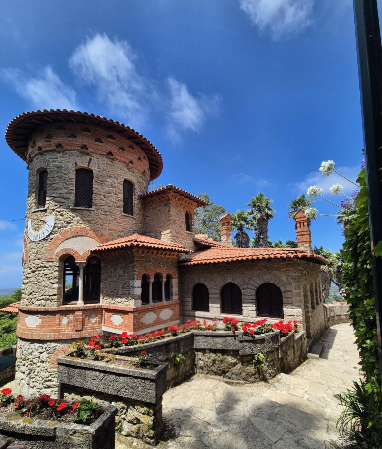 Villa Sassetti in Sintra featuring a round tower with arched windows, terracotta roof tiles, and stone walls, set among manicured gardens and a stone path.