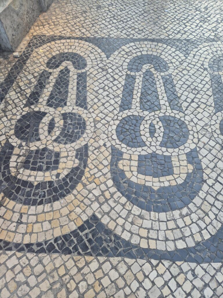 A section of Portuguese pavement featuring a symmetrical black and white tile pattern resembling stylized keys or abstract figures.