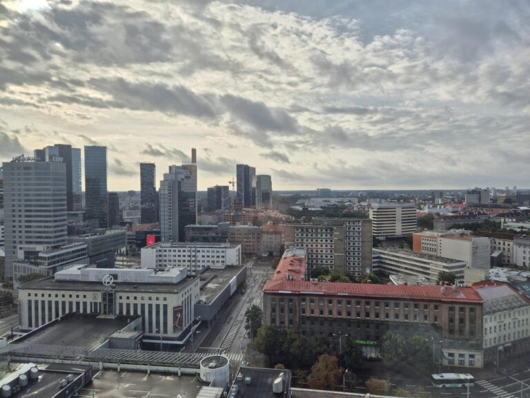 Panoramic city view from the 21st floor of Sokos Hotel Viru, showing a mix of modern high-rises and historic red-roofed buildings under a partly cloudy sky.