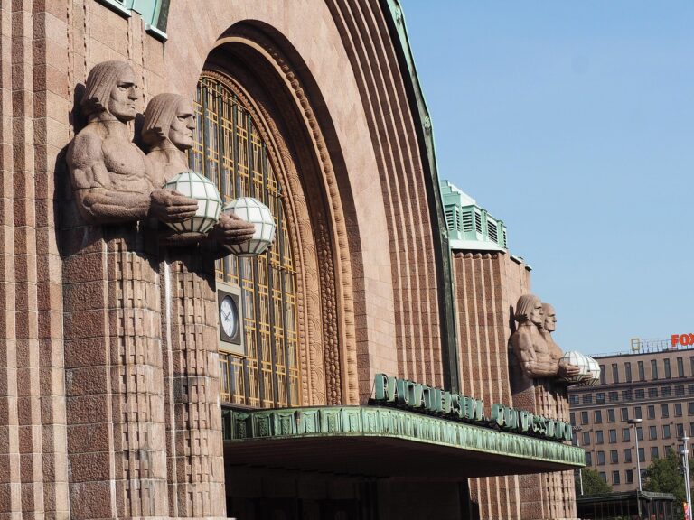 Stone statues holding spherical lamps at the entrance of Helsinki Central Railway Station.