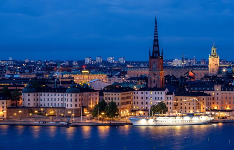 Night view of Stockholm waterfront with illuminated buildings and church spire.