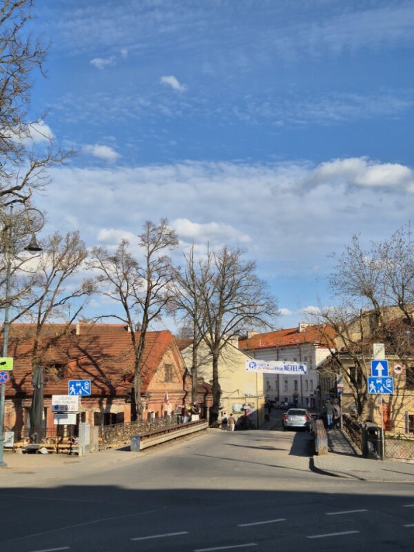 Street leading toward Užupis with bridge railings, rooftops, and road signs.
