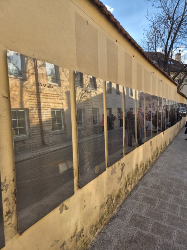 Long wall with mirrored plaques displaying text along a sidewalk.